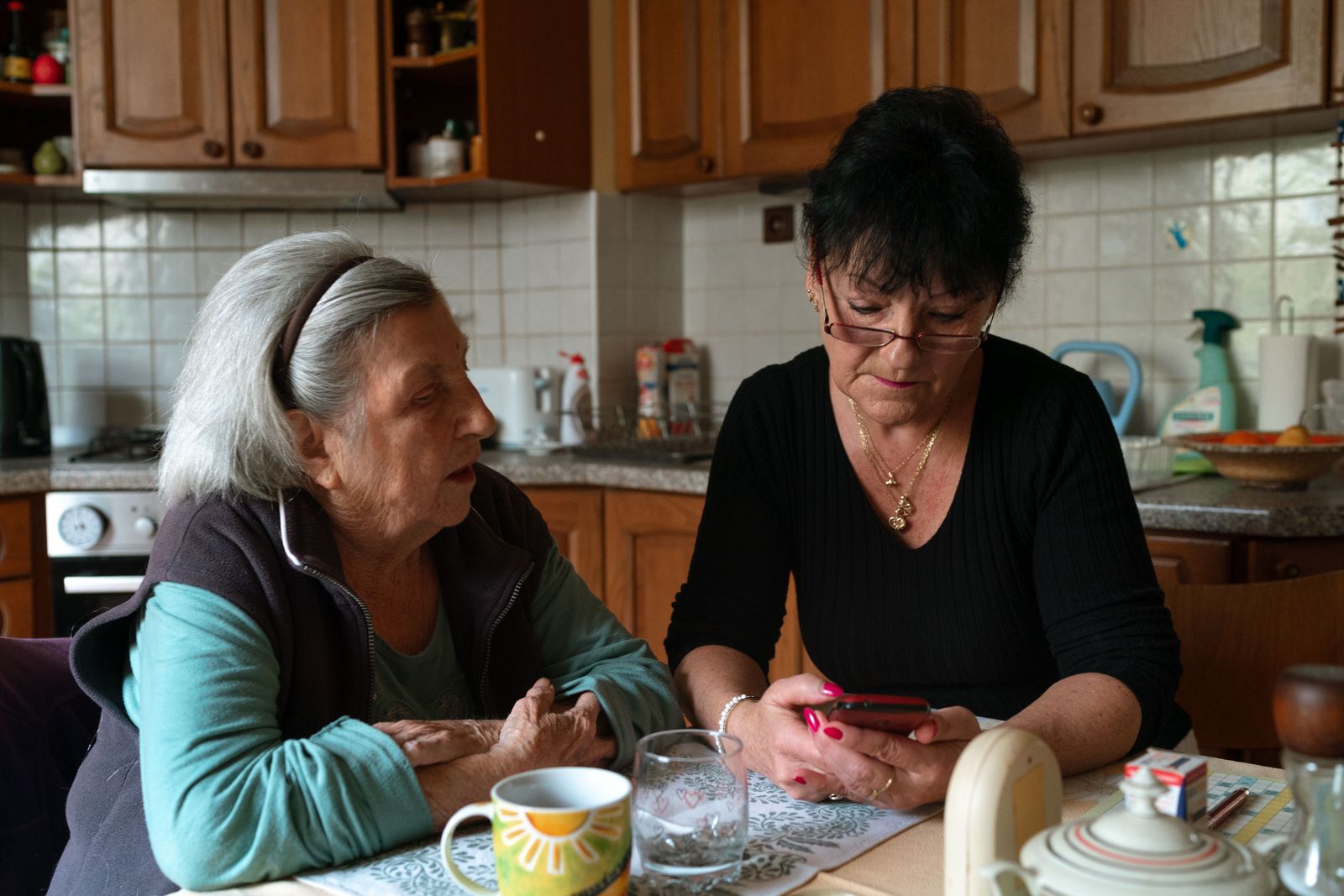A caregiver and an older woman chatting at her kitchen table over a cup of tea